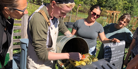 Four people participate in a composting demonstration outdoors