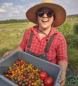 Laura Fredrickson-Gosewisch, Minnesota vegetable farmer, stands in a field holding a crate of tomatoes