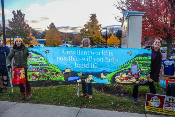 Three people outside holding a banner that says "A resilient world is possible - will you help build it?"