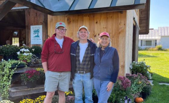 Three people pose outside a Vermont Land Trust farm market shed